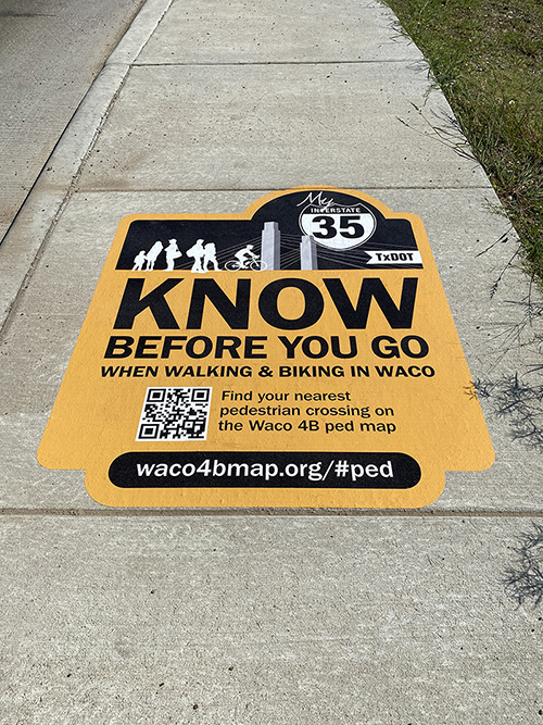 A know-before-you-go decal installed on a sidewalk. Billboard text: Know before you go when walking and biking in waco. Find the nearest pedestrian crossing on the Waco 4B ped map - waco4bmap.org/#ped